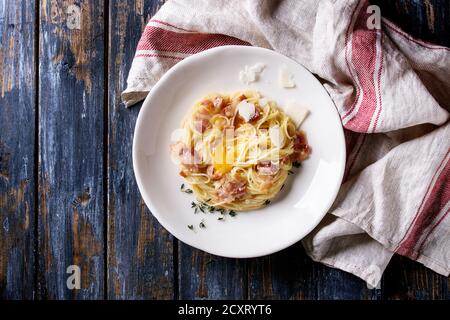 Traditionellen italienischen Pasta alla Carbonara mit Eigelb, bauchspeck Speck, Parmesan, Thymian, in weißen Teller serviert auf Textilien Bettwäsche über alte Holz- Pla Stockfoto