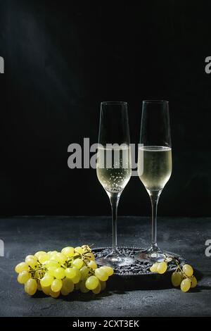 Zwei Gläser Champagner weiß auf schwarz Holz Dekorative Vorstand mit grünen Trauben über dunkle Textur Hintergrund serviert. Platz kopieren Stockfoto