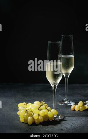 Zwei Gläser Champagner weiß mit grünen Trauben über dunkle Textur Hintergrund serviert. Platz kopieren Stockfoto