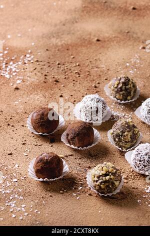 Vielfalt an hausgemachten dunklen Schokoladentrüffeln mit Kakaopulver, Kokosnuss, Walnüssen über Kakaopulver als Hintergrund. Speicherplatz kopieren. Stockfoto