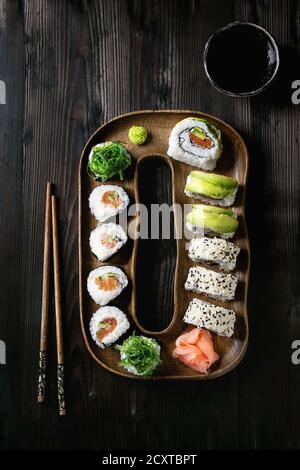 Hausgemachte sushi Brötchen mit Lachs, Sesam und Avocado in Holz Platte serviert mit Rosa eingelegter Ingwer, Sojasauce, Wasabi, Algensalat, Koteletts Stockfoto