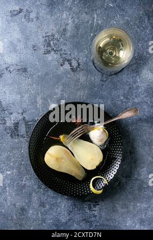 Traditionelle Dessert geschnitten pochierte Birnen in Weißwein in schwarze Platte mit Sirup serviert, Eis, Zitronenschale und Glas Weißwein über Blau textu Stockfoto