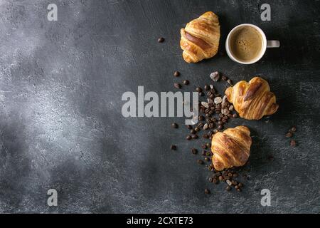 Frisch gebackene Croissants und traditionelle Tasse Espresso Kaffee, Kaffeebohnen, Zucker über schwarzen Textur Hintergrund. Ansicht von oben, kopieren Raum Stockfoto