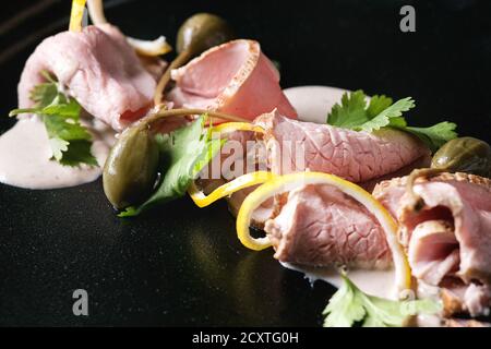 Vitello Tonnato italienische Gericht. Dünn geschnittenes Kalbfleisch mit Thunfisch Soße, Kapern und Koriander auf schwarzem Teller serviert. Nahaufnahme Stockfoto