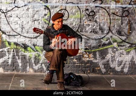 London, Großbritannien - 14. September 2017: Musiker sitzt und spielt klassische Gitarre auf der Straße in der Nähe der Wand voller Graffiti Stockfoto
