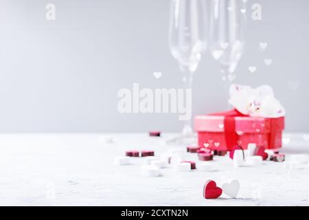 Liebe Valentinstag Grußkarte mit zwei leeren Champagner Gläser, roter Geschenkbox mit Orchidee und hölzerne Herz über weiß grau hinterlegt. Kopieren Stockfoto