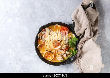 Pasta Spaghetti Vongole in Tomaten-Sahne-Sauce in gusseisernen Pfanne mit textilen über grau Textur Hintergrund. Ansicht von oben, Raum Stockfoto