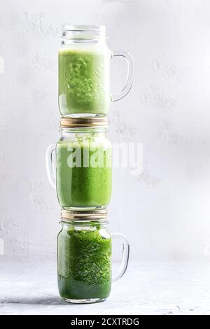 Vielzahl von drei Farbe grün Spinat kale apple Joghurt Smoothie in Maurergläser auf jedem Anderen über grauen Hintergrund. Detox gesund vegan zu essen. Stockfoto