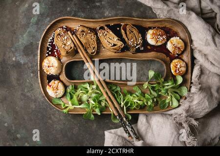 Im asiatischen Stil gebratene Jakobsmuscheln mit japanischem Omelett gerollt Tamagoyaki und Sesam Soja Sauce in Holzplatte mit grünem Salat, Essstäbchen, Textil Serviette Stockfoto