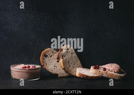 Huhn hausgemachter Leberpastete oder Pastete mit in Scheiben Vollkornbrot und Preiselbeeren im Glas über dunkle Textur Hintergrund serviert. Platz kopieren Stockfoto