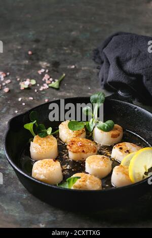 Gebratene Jakobsmuscheln mit Butter Zitrone pikante Sauce aus Guss mit grünem Salat und textile Serviette über Altes, dunkles Metall Hintergrund serviert pan. Stockfoto