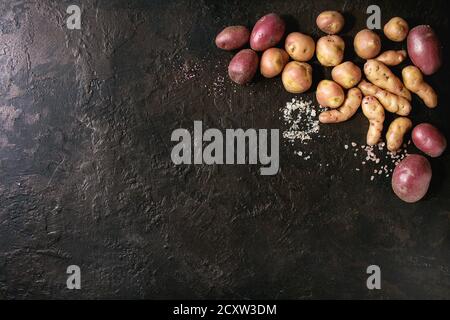 Vielzahl von Roh ungekocht Biokartoffeln unterschiedlicher Art und Farben Rot, Gelb, Lila mit verschiedenen von Salz über dunkle Textur Hintergrund. Ansicht von oben, Co Stockfoto