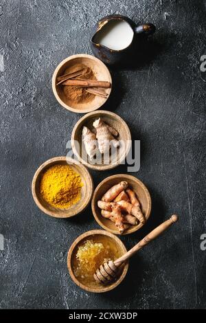 Zutaten für gelbwurz Latte. Boden Gelbwurz, curcuma root, Zimt, Ingwer, Bienenwaben in Holzschalen, Kanne Milch über schwarze Textur Hintergrund Stockfoto