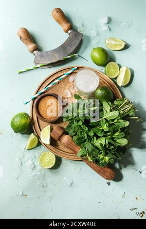 Zutaten für die Herstellung von mojito Cocktail. Frische Minze, Limette, brauner Zucker, crashed ice cubes, Glas Sodawasser, cocktail Rohre auf Holzbrett über gr Stockfoto