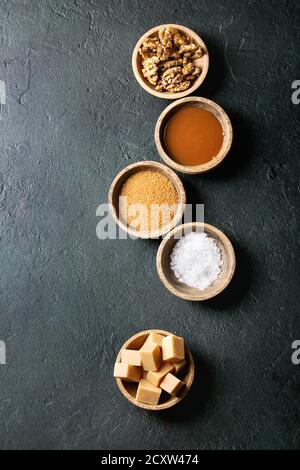 Gesalzene caramel fudge Bonbons mit Fleur de Sel, Karamell Sauce serviert, braunen Rohrzucker und karamellisierte Walnüsse in Holz Schalen über schwarzen Textur backgrou Stockfoto