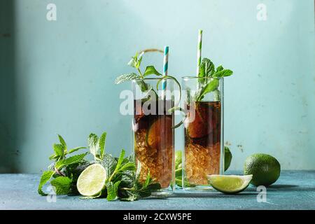 Zwei Gläser classic Cuba Libre Cocktail mit Limetten, Minze, crushed Eis und Cola, serviert mit Zutaten oben und retro cocktail Rohre über Türkis Stockfoto