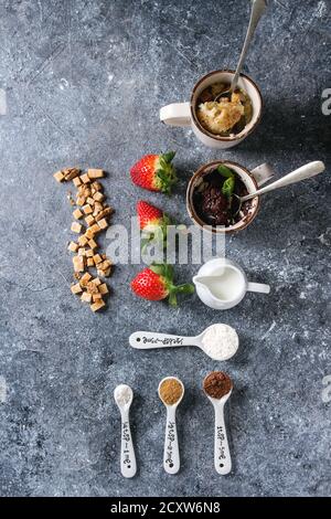 Schokolade und Vanille Karamell Becher Kuchen aus der Mikrowelle mit frischen Erdbeeren und Inhaltsstoffe in Löffel über blaue Textur Hintergrund. Ansicht von oben, Stockfoto