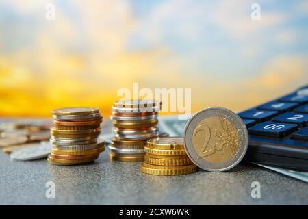 Münzen in Haufen und ein Taschenrechner auf einem Sonnenaufgangshintergrund. Kostengünstiges Konzept. Stockfoto