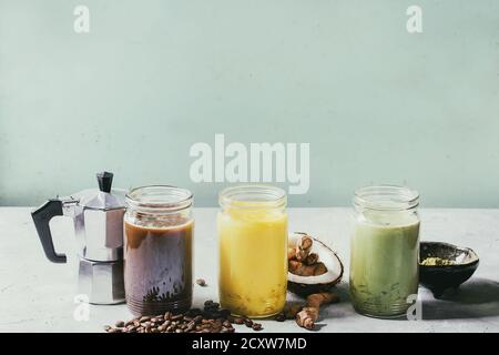 Vielzahl von bunten Iced Latte Getränke. Eiskaffee, Kurkuma und Matcha Latte Cocktails in Gläsern mit Zutaten oben über Grau Grün Textur b Stockfoto