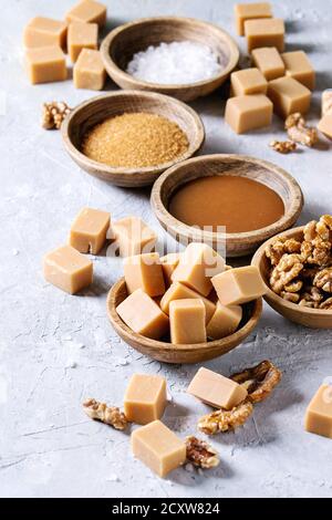 Gesalzene caramel fudge Bonbons mit Fleur de Sel, Karamell Sauce serviert, braunen Rohrzucker und karamellisierte Walnüsse in Holz Schalen über grau Textur backgroun Stockfoto