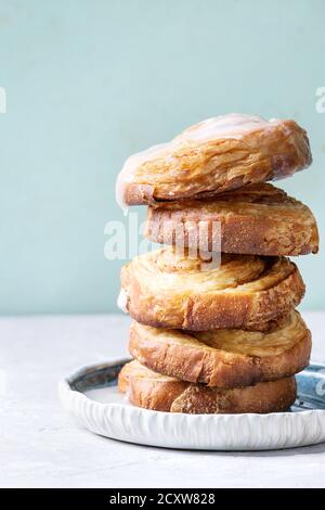 Stapel von hausgemachten verglaste Blätterteig Zimtschnecken mit Vanillesauce und Rosinen auf blauen Platte über Grau grün Hintergrund. Pin-up-Stil, kopieren Raum Stockfoto