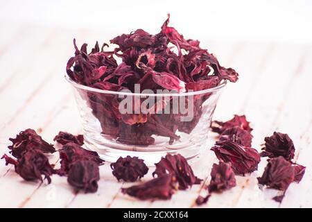 Trockene Blüten von Hibiscus sabdariffa (Roselle, Karkade) in Glasschale auf rustikalem weißen Hintergrund. Stockfoto