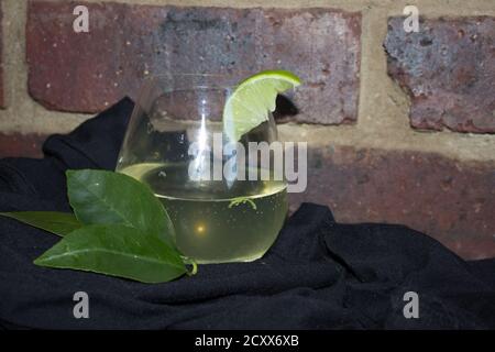 Gin und Tonic auf einem schwarzen Material gegen eine rustikale Ziegelwand, mit garniert mit einem Stück Limette Stockfoto