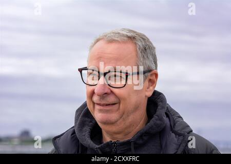 Nahaufnahme eines Mannes mittleren Alters, um die 50, mit grauen Haaren und Brille. Blauer Dunsthimmel im Hintergrund Stockfoto