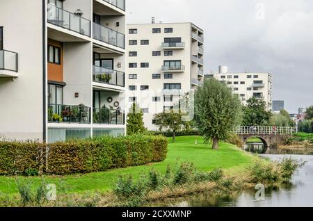 Spijkenisse, Niederlande, 30. September 2020: Gruppe von drei weiß verputzten Wohngebäuden in einer parkähnlichen Umgebung neben einem Kanal Stockfoto