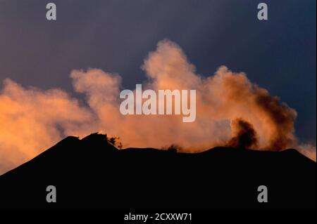 Strahlen der sinkenden Sonne färben hinterleuchtete Rauchwolken und schwebende Schwefelgaswolken von Gipfelkratern auf dem Ätna, Sizilien, Italien, in dieser Ansicht aus dem Osten im August 2011. Der Ätna ist der höchste aktive Vulkan Westeuropas. Die Aktivität begann vor 500,000 Jahren mit vielen hochexplosiven Eruptionen seitdem. Seit 1600 gab es 60 Eruptionen durch Seitenschlitze und viele weitere vom Gipfel, einschließlich jener in den Jahren 2006, 2007-8, 2012 und 2018. Ätna war ziemlich ruhig im Jahr 2011, aber intensive Aktivität ab Januar 2012 zwang die vorübergehende Schließung des Catania International Airport. Stockfoto