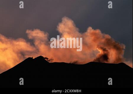 Strahlen der sinkenden Sonne färben hinterleuchtete Rauchwolken und schwebende Schwefelgaswolken von Gipfelkratern auf dem Ätna, Sizilien, Italien, in dieser Ansicht aus dem Osten im August 2011. Der Ätna ist der höchste aktive Vulkan Westeuropas. Die Aktivität begann vor 500,000 Jahren mit vielen hochexplosiven Eruptionen seitdem. Seit 1600 gab es 60 Eruptionen durch Seitenschlitze und viele weitere vom Gipfel, einschließlich jener in den Jahren 2006, 2007-8, 2012 und 2018. Ätna war ziemlich ruhig im Jahr 2011, aber intensive Aktivität ab Januar 2012 zwang die vorübergehende Schließung des Catania International Airport. Stockfoto