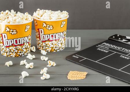 Nahaufnahme, Popcorn-Eimer neben einem Klappbrett und Kinokarten, auf grauem Hintergrund. Konzepte, selektiver Fokus, Film- und Fernsehindustrie Stockfoto