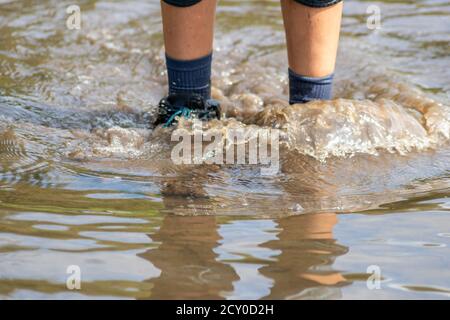 Kleiner Junge waten durch Flut mit blauen Gummistiefel nach Eine Überschwemmung hat den Schutzdeich durchbrochen und die überschwemmt niederlande oder Küste des Ozeans Stockfoto