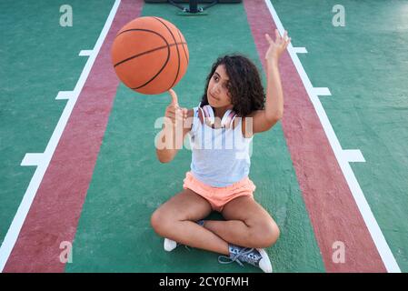 Ein kleines Mädchen, das sich hinsitzt, dreht einen Korbball. Lifestyle-Konzept Stockfoto