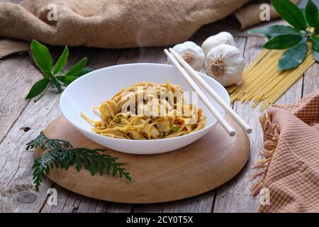 Asiatische Küche - bami Goreng Nudeln auf rustikalem Hintergrund und Essstäbchen Stockfoto