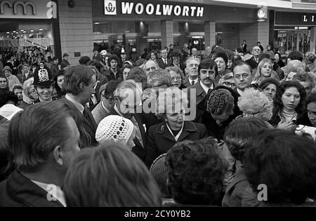 AJAXNETPHOTO, 11. FEBRUAR 1977. PORTSMOUTH, ENGLAND. - RUNDGANG DURCH DIE STADT - FRAU MARGARET THATCHER (CON), OPPOSITIONSFÜHRERIN, SETZT SICH WÄHREND EINER WAHLKAMPFTOUR MIT DER ÖFFENTLICHKEIT IM EINKAUFSVIERTEL DER HANDELSSTRASSEN AUSEINANDER. IHR MANN DENIS STEHT RECHTS VON FRAU THATCHER. FOTO: JONATHAN EASTLAND/AJAX REF:3771102 46 Stockfoto