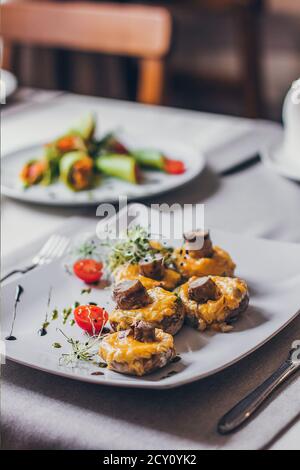 Gefüllte Pilze gefüllt mit Käse, Pilzstielen, frischen Kirschtomaten und Microgreen. Stockfoto