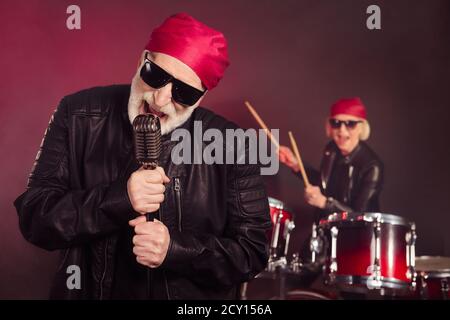 Foto von pensionierten energischen Dame Mann beliebten Rock-Gruppe spielen Drum Instrument singen berühmten Song Konzert Performance tragen Rocker Leder Kleidung Bandana Stockfoto