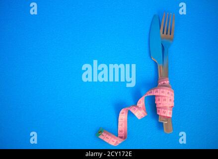 Gabel und Messer sind in rosa Maßband eingewickelt Auf blauem Hintergrund Stockfoto