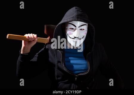 Mann bewaffnet mit einer Axt und trägt eine Maske und einen Hoodie auf schwarzem Hintergrund. Stockfoto