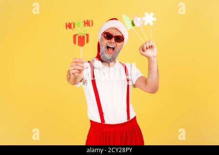 Extrem positiv aufgeregt grauen bärtigen erwachsenen Mann in roten Hut hält Glückwunschkarten auf Sticks, Neujahr und weihnachtsfeier. innenstudi Stockfoto