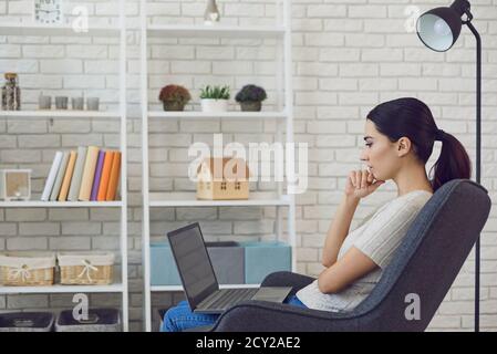 Nachdenkliche junge Geschäftsfrau mit Laptop-Computer von zu Hause. Seitenansicht des Freiberuflers, der in Innenräumen an einem neuen Projekt arbeitet Stockfoto