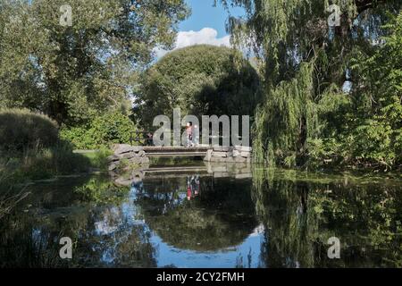 Brücke über einen Teich am Seitenarm des Rideau-Kanals, mit Spaziergängern. Große Weide reflektiert auf der Seite Stockfoto