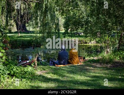 Ehepaar von hinten gesehen, sitzt unter Bäumen an einem Teich, einem Seitenarm des Rideau-Kanals Stockfoto