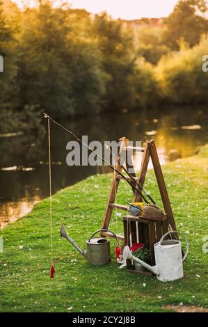 Wunderschönes Dekor mit alten Gießkannen, Holzleiter und Regalen am Fluss. Stockfoto