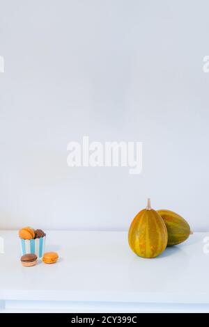 Minimalistisches Halloween-Konzept - Süßigkeiten, Makarons Dessert in einem Papierbecher und dekorative Kürbisse. Schokolade und Kürbismakronen auf weißem Hintergrund Stockfoto