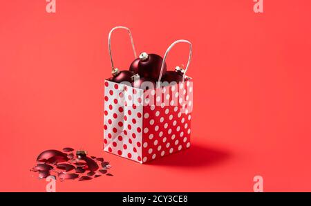 Weihnachts-Einkaufstasche voller roter Kugeln, isoliert auf einem roten nahtlosen Hintergrund. Rote Weihnachtskugeln in einer Geschenktüte. Holiday Shopping Konzept. Stockfoto