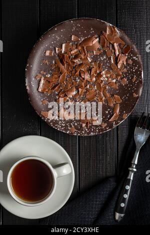 Süßer Schokoladenkäse-Kuchen und Teetasse auf schwarzem Holztisch. Draufsicht. Stockfoto