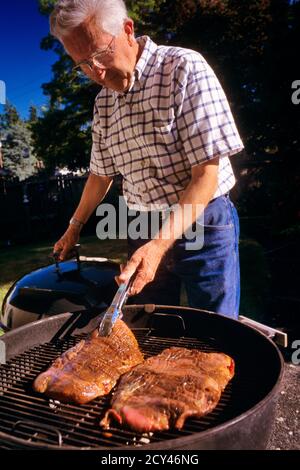 80ER JAHRE SENIOR MANN KOCHEN STEAKS AUF GRILL - KC12986 LGA001 HARS ERWACHSENE MÄNNER VERTRAUEN SENIOR MANN SENIOR ERWACHSENE ZIELE ERHOLUNG CAMPING GESCHICKLICHKEIT AKTIVITÄT UNTERHALTUNG GRILLEN ALTER OLDSTERS HOCH WINKEL OLDSTER HOBBY INTERESSE HOBBYS WISSEN ERHOLUNG ZEITVERTREIB FREUDE ELDERS NAHRUNG PICKNICK BAR-B-QUE ENTSPANNUNG STEAKS AMATEUR KAUKASISCHEN ETHNIE GENUSS DIE ZUBEREITUNG DER SPEISEN WAR ALTMODISCH Stockfoto