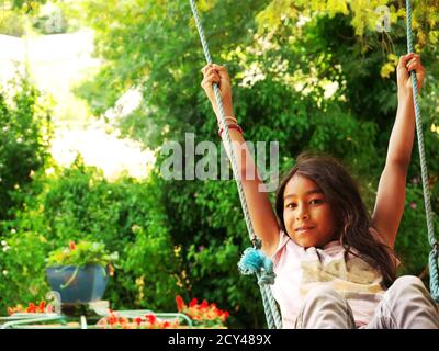 Junge lächelnde Mixed-Race-Mädchen schwingt in einem Park während der Urlaub Stockfoto